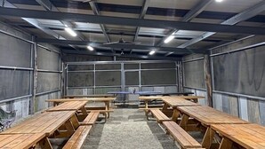 A spacious indoor area with high ceilings, metal walls, and multiple wooden tables and benches arranged for seating. - GROUP CAMP ON MURRAY RIVER NEAR ECHUCA / MOAMA (Torrumbarry)