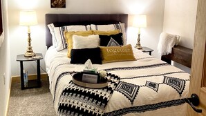 Una camera da letto ordinata con un letto a castello, un comodino con una lampada e un vassoio decorativo con un cartello.