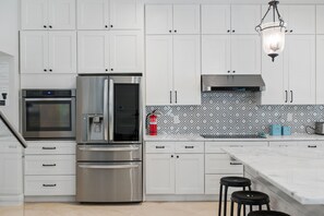 Una cocina moderna con armarios blancos, electrodomésticos de acero inoxidable, un salpicadero estampado y una isla de mármol.