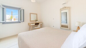 Un dormitorio con cama, escritorio, silla, espejo y ventana con vista a un puente.