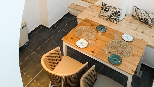 Un espacio moderno para comer al aire libre, con una mesa de madera, sillas de mimbre y vistas a una piscina.