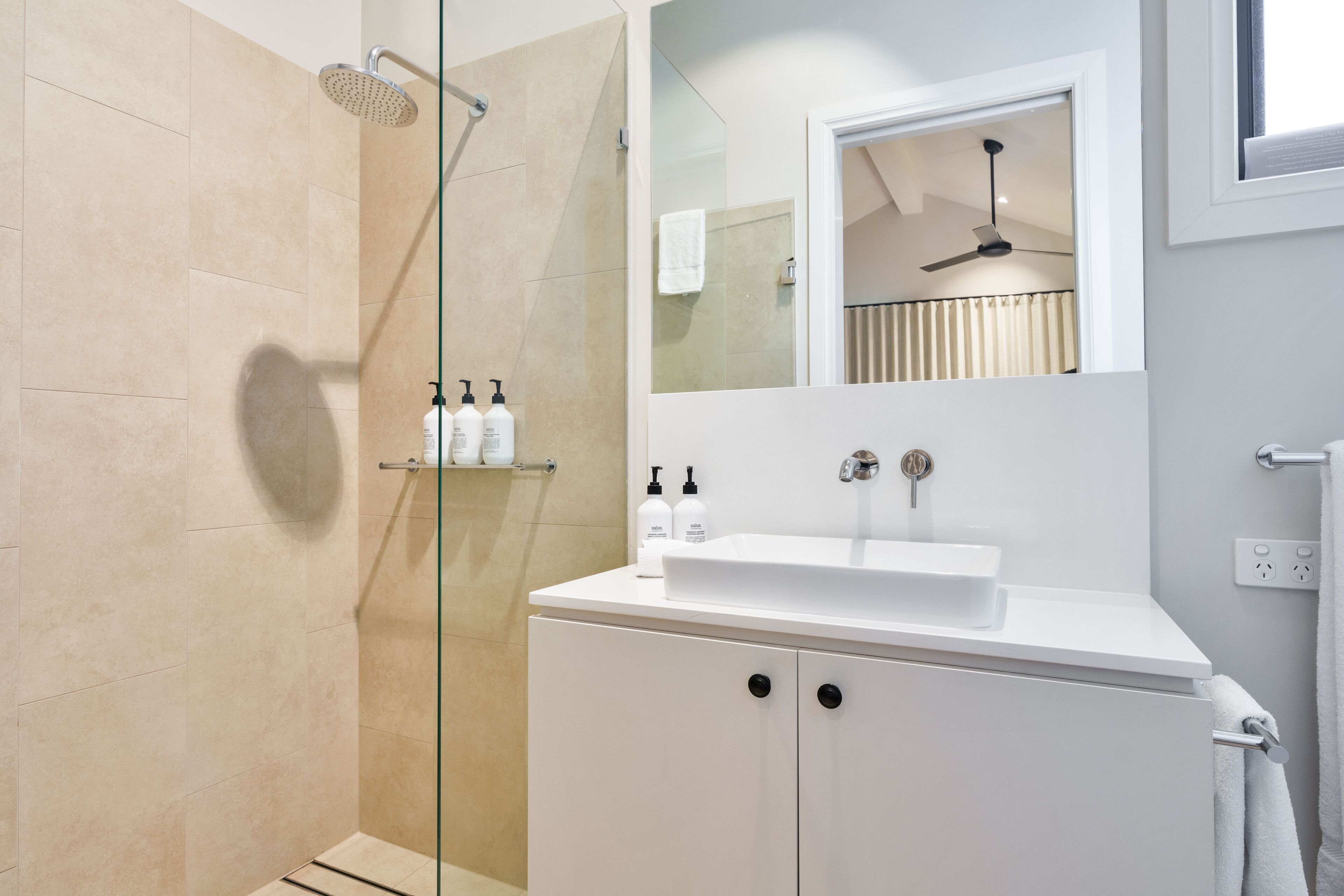 Un bagno moderno con cabina doccia in vetro, un lavandino bianco e uno specchio sopra il lavandino.