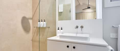Un bagno moderno con cabina doccia in vetro, un lavandino bianco e uno specchio sopra il lavandino.
