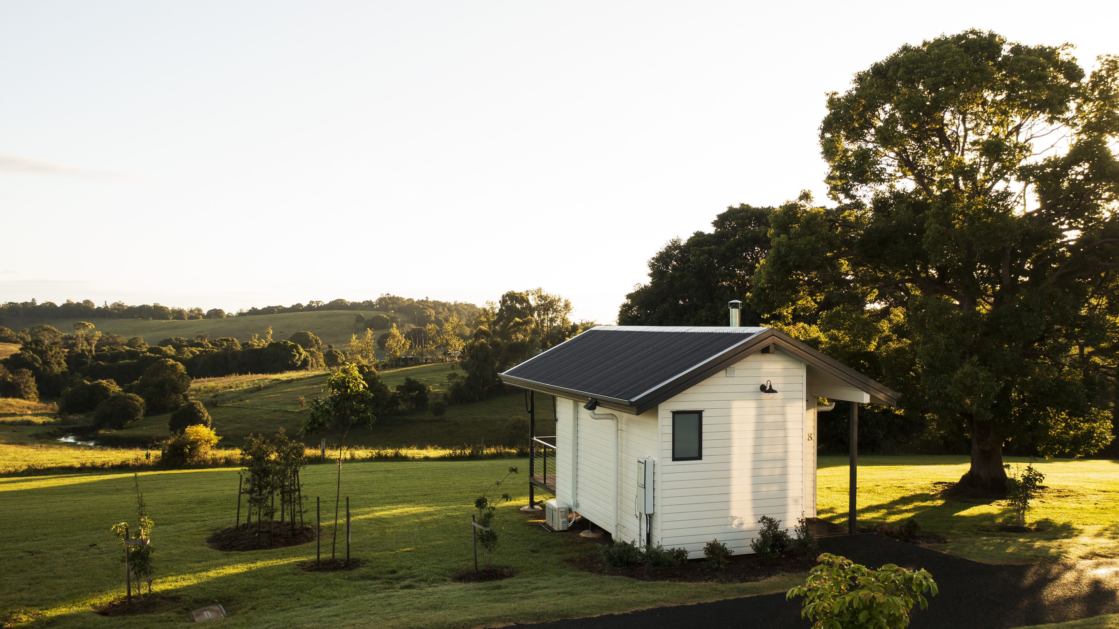A small white house with a dark roof, surrounded by a grassy field and trees.