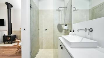 A modern bathroom with a white sink, glass shower enclosure, and a black wood-burning stove.