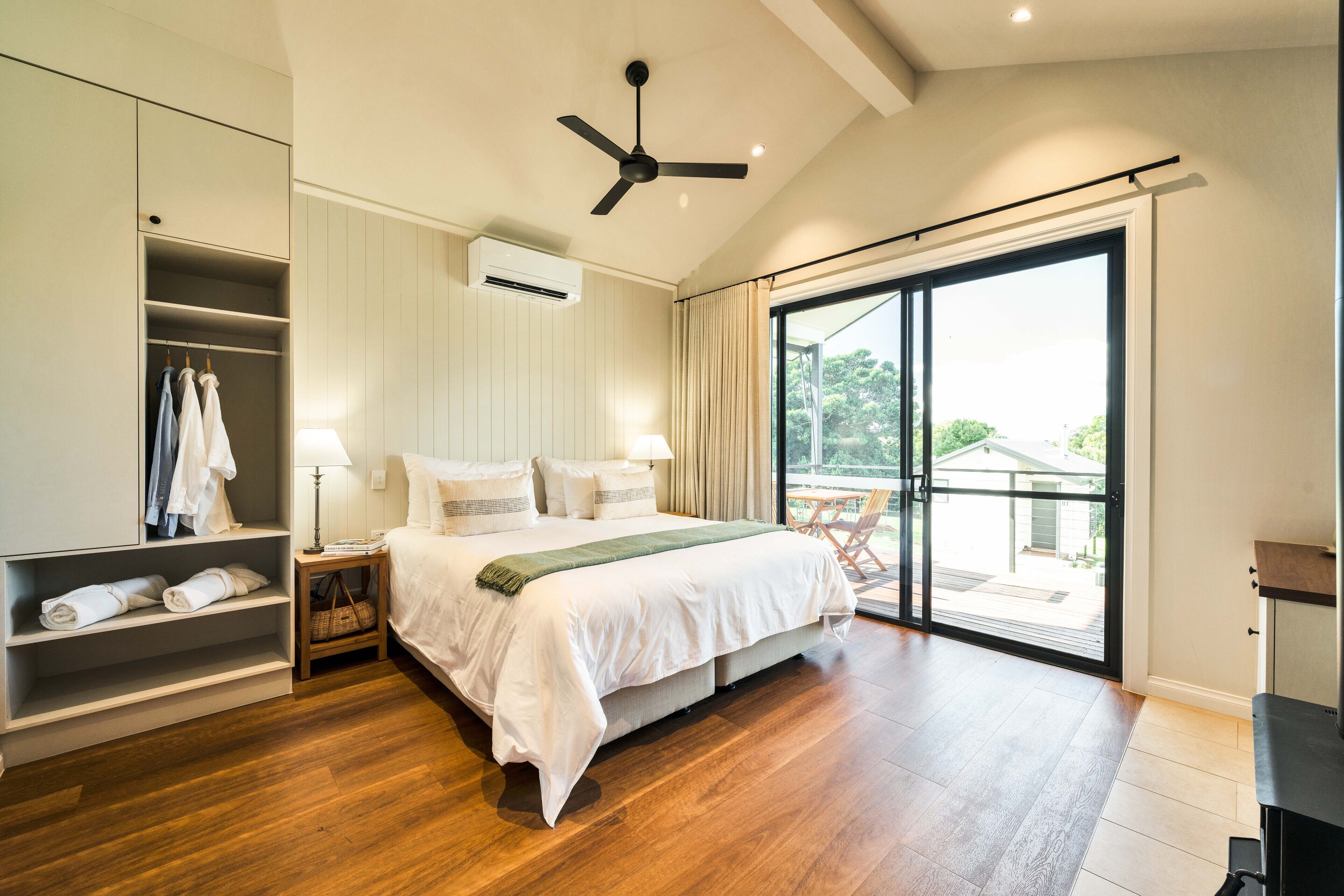 Une chambre à coucher comprenant un lit, une armoire, une table de chevet, une lampe et une porte-fenêtre coulissante donnant sur un balcon.