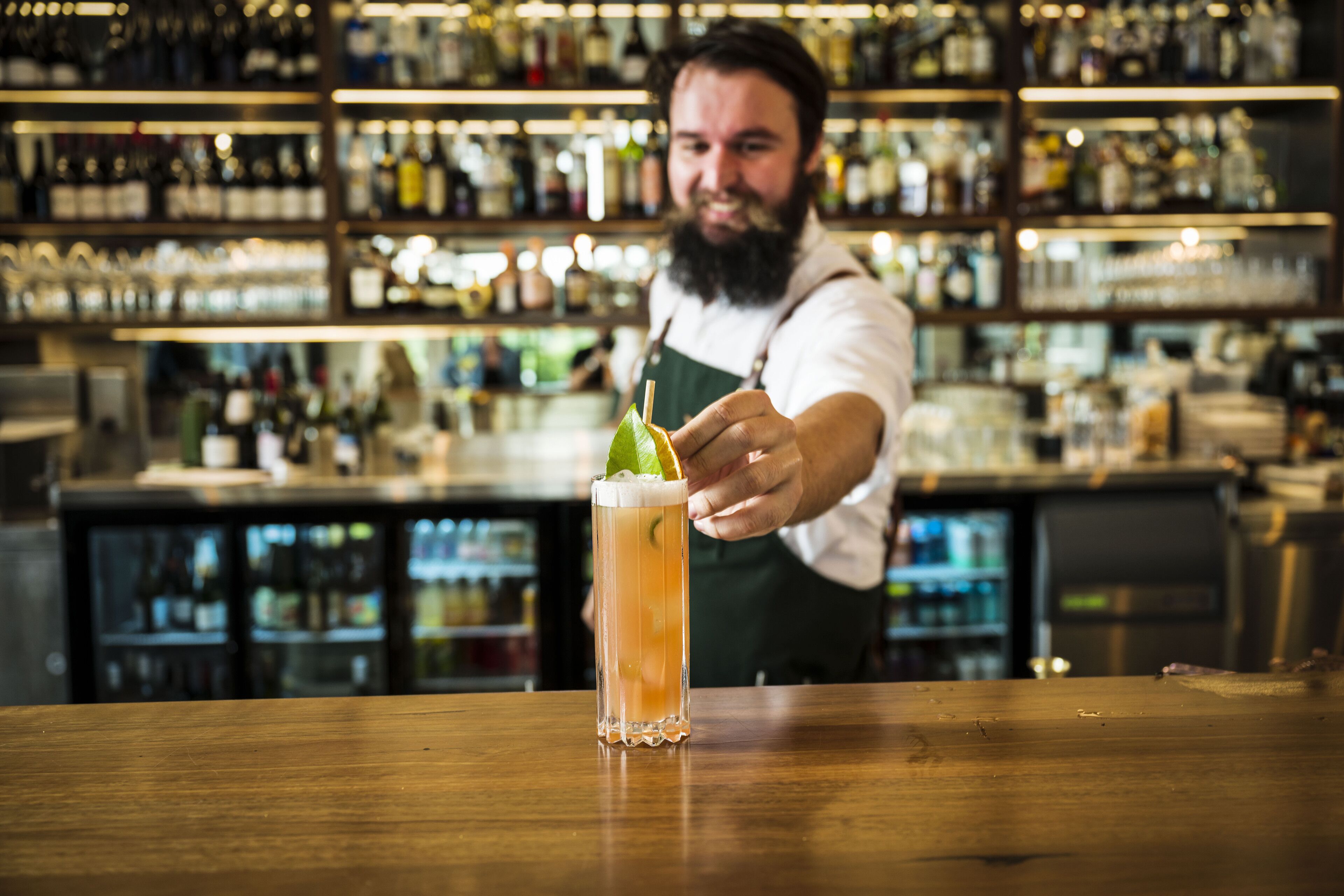 A bartender at a bar with a tall glass of a beverage garnished with a lime.