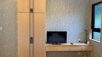 Une chambre avec une armoire en bois, un téléviseur posé sur un bureau en bois, une fenêtre et une poubelle.