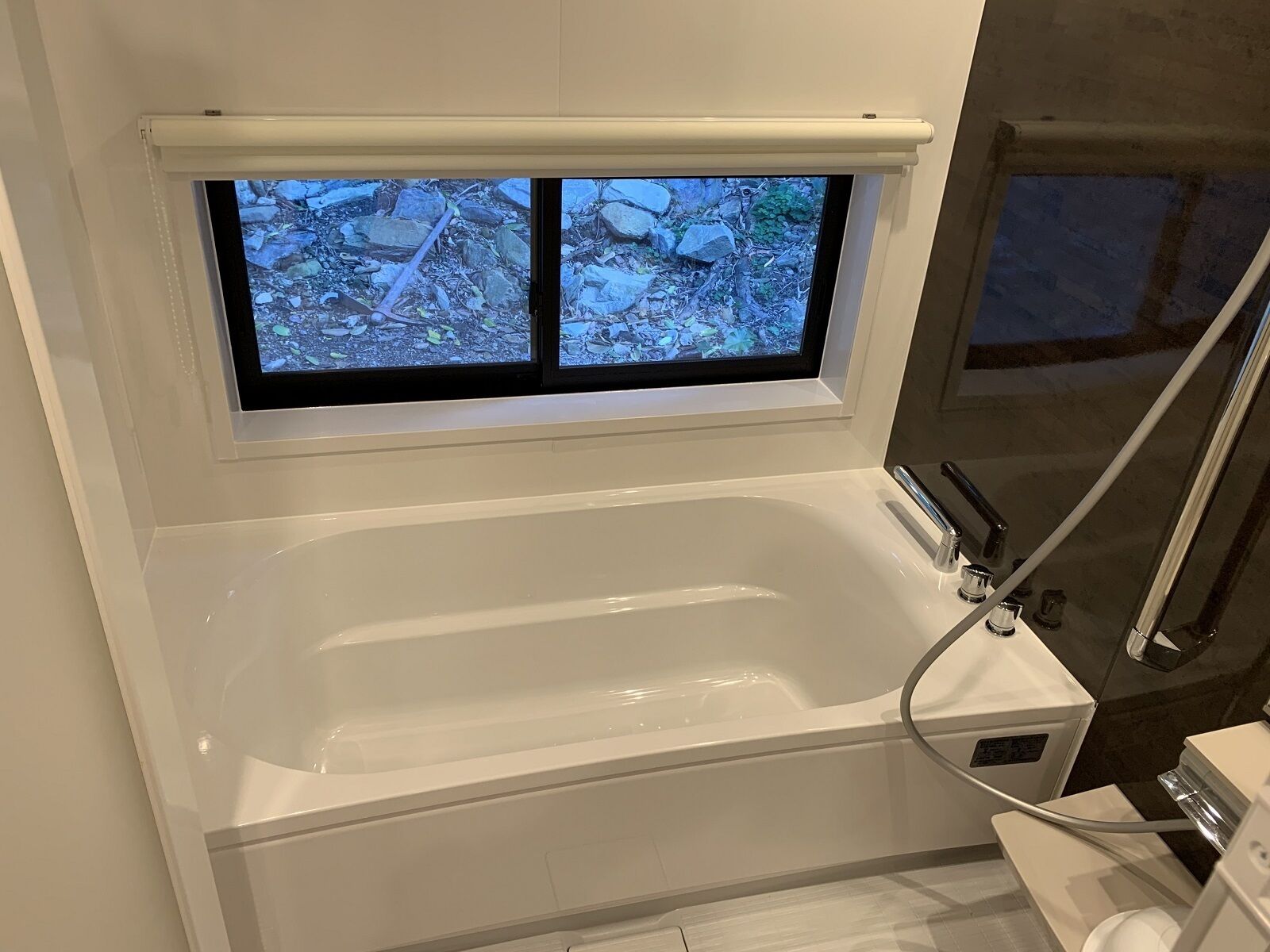 A modern bathroom with a bathtub, a window with a view of a rocky outdoor area, and a shower area.