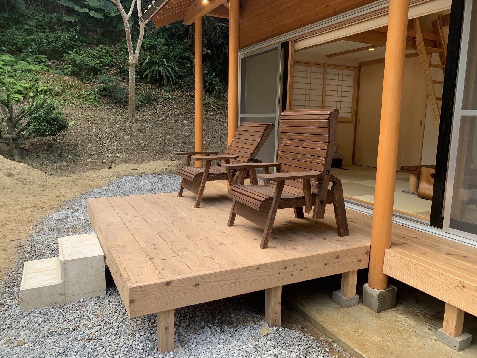 Una terraza de madera con dos sillas de madera y un banco de hormigón.