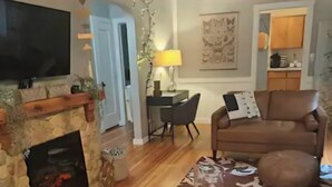 Un salon doté d’une cheminée en pierre, d’un canapé en cuir marron, d’un tapis à motifs et d’un téléviseur fixé au mur.