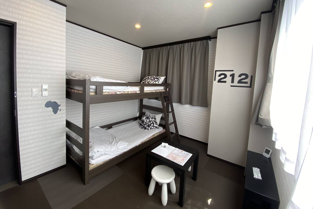A bunk bed room with a desk and chair, a window with curtains, and a wall with a number.