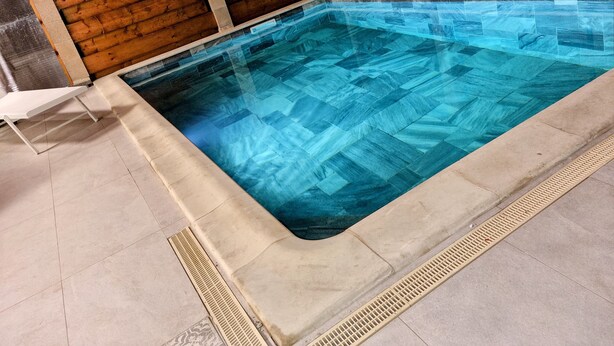 A rectangular swimming pool with clear blue water, surrounded by a tiled deck and a wooden fence.