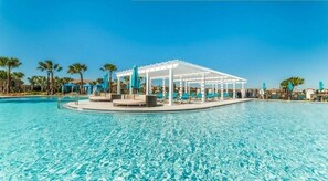 En klarblå pool med ett vitt lusthus och solstolar.