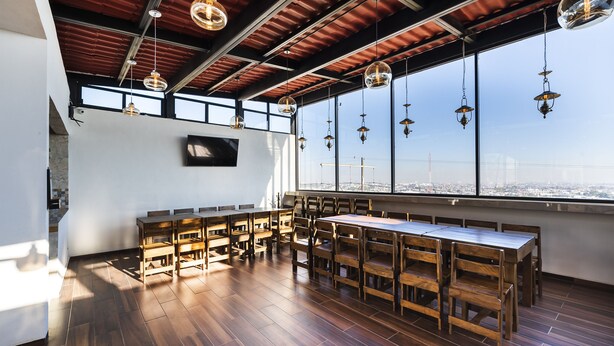 Un comedor amplio con mesas y sillas de madera, ventanas grandes con vistas a la ciudad y lámparas colgantes.