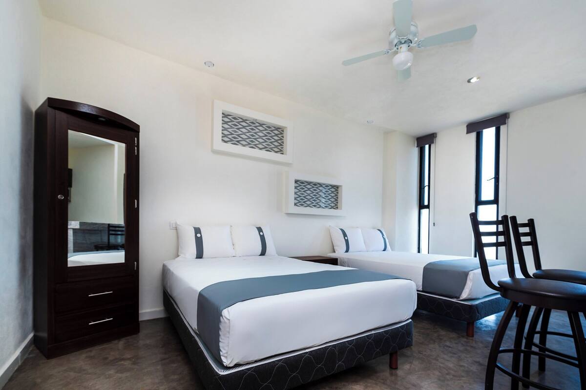 Une chambre d’hôtel avec deux lits, un grand miroir, un ventilateur de plafond et une fenêtre donnant sur un beau paysage.