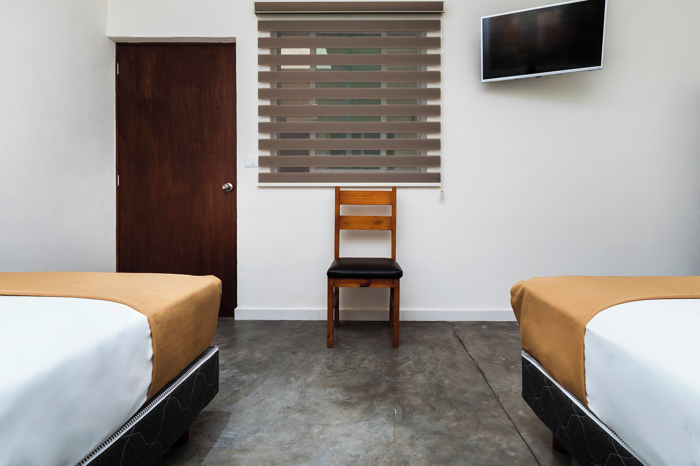 A hotel room with two beds, a wooden chair, a TV, and a window with blinds.