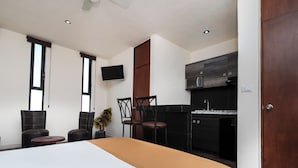 Una habitación de hotel moderna con una cama grande, un televisor, una zona de cocina y dos sillas.
