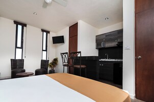 Una habitación de hotel moderna con una cama grande, un televisor, una zona de cocina y dos sillas.