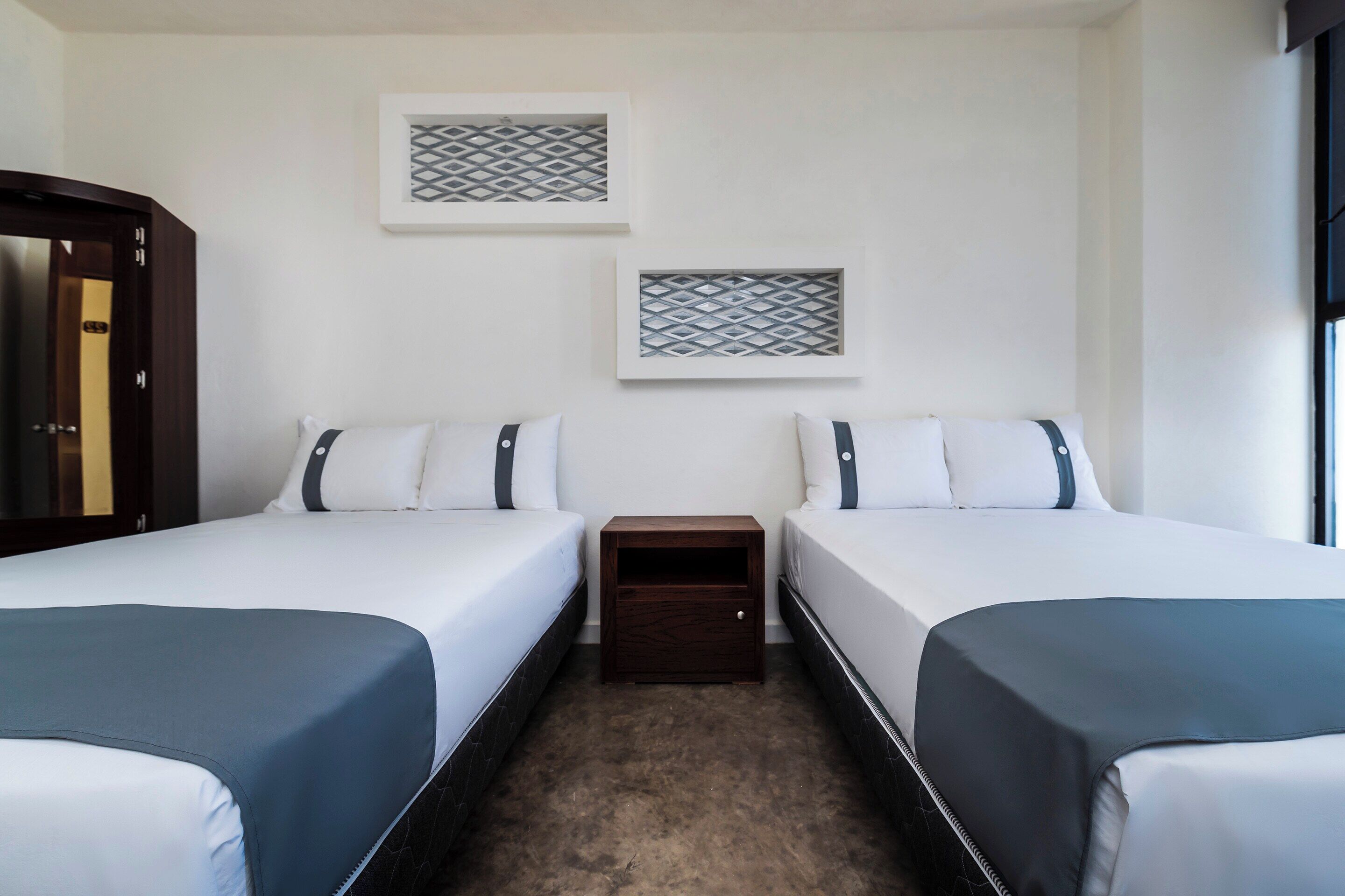 A hotel room with two beds, a nightstand, and two wall-mounted decorative items.