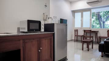 Cozinha com micro-ondas, geladeira e máquina de café no balcão. Há armários de madeira e uma janela com vista para árvores.