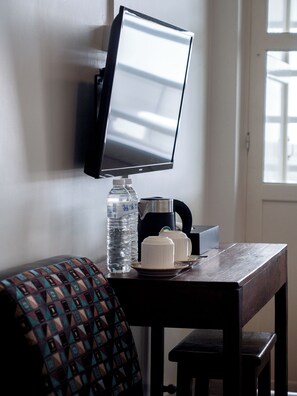 A room with a mounted television, a water bottle, a coffee maker, and a small table with cups. - Niagara Hotel (Bang Rak)
