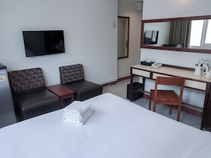 A hotel room with a bed, a desk, a chair, a TV, and a small kitchenette. - Niagara Hotel (Bangkok)