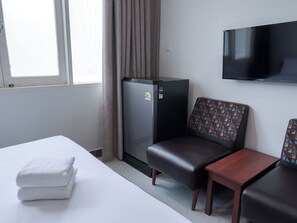 A hotel room with a bed, a small table, a sofa, a television, and a refrigerator. - Niagara Hotel (Bangkok)