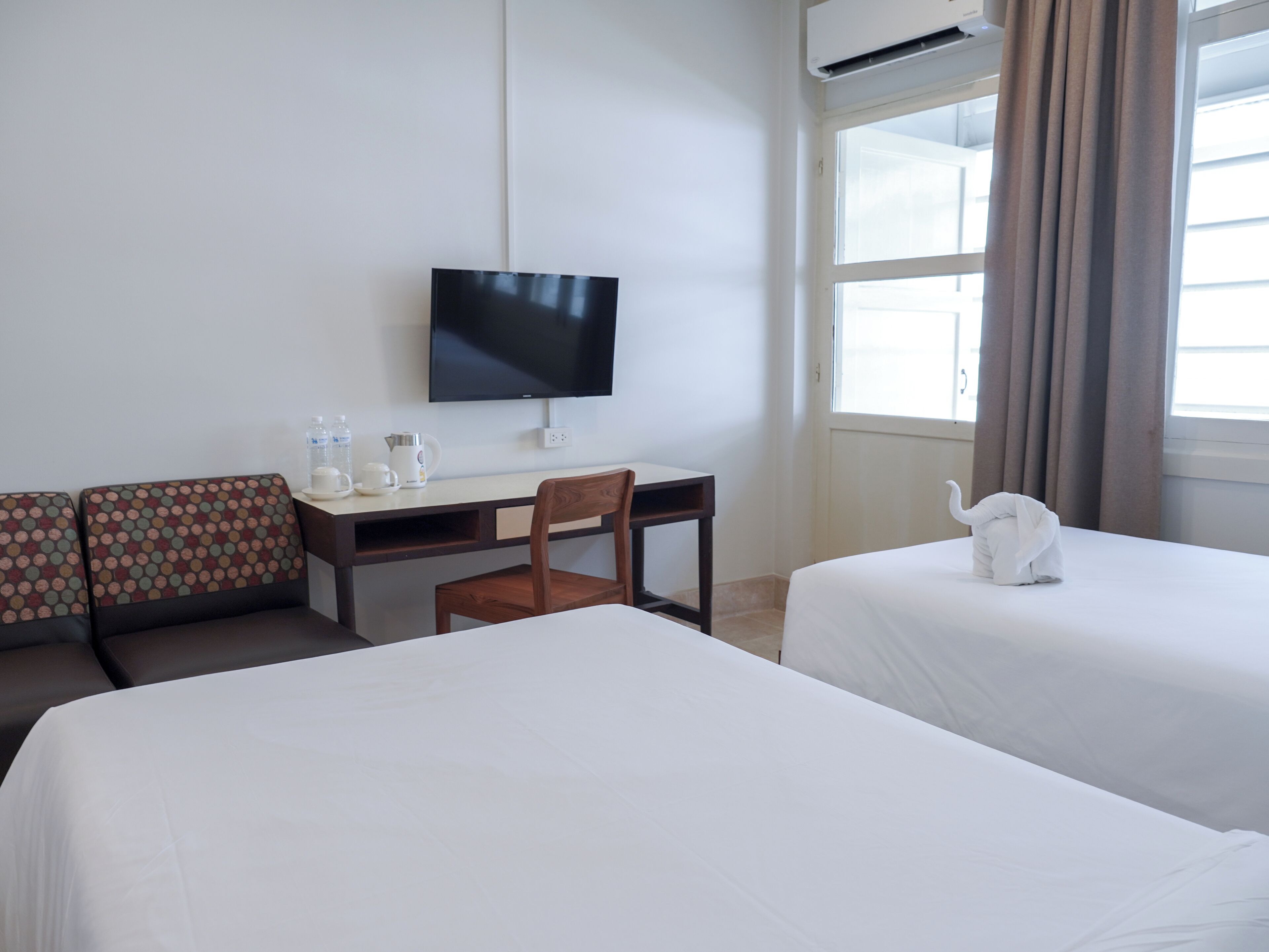 Ein Hotelzimmer mit zwei Betten, einem Schreibtisch mit Stuhl, einem Fernseher und einem Fenster mit Vorhängen.
