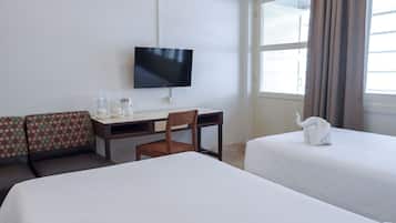 Habitación de hotel con dos camas, un escritorio con silla, televisor y ventana con cortinas.