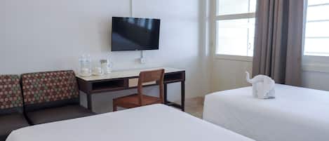 Une chambre d’hôtel avec deux lits, un bureau avec une chaise, une télévision et une fenêtre avec des rideaux.