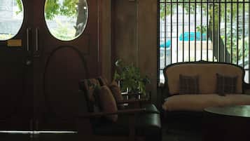Quarto com sofá, uma cadeira, mesa redonda e planta em vaso. Duas janelas oferecem vista para o exterior.