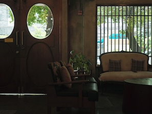 A room with a sofa, a chair, a round table, and a potted plant. There are two windows with a view of the outside. - Niagara Hotel (Bangkok)