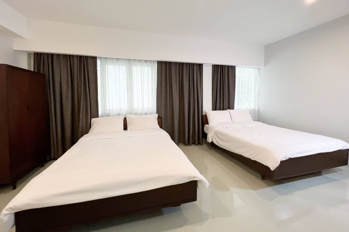 A hotel room with two beds, a wardrobe, and a large window with curtains.