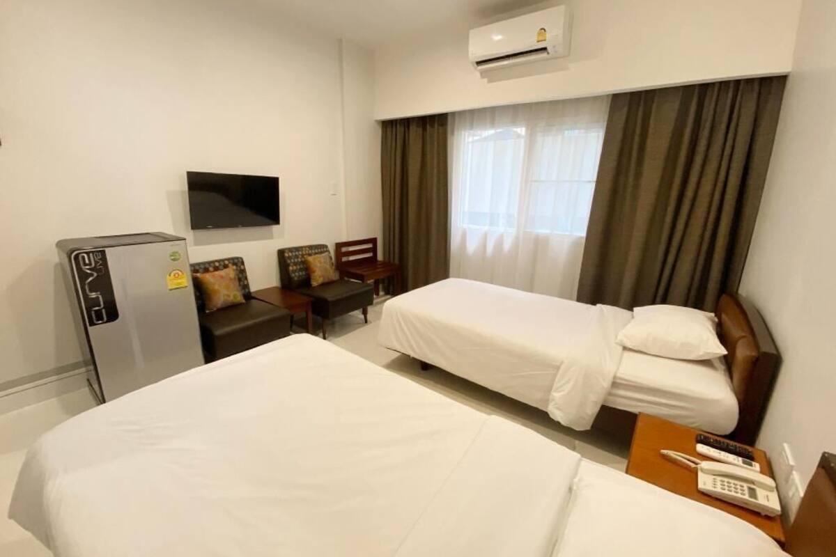 A hotel room with two beds, a TV, a desk, and an air conditioning unit.