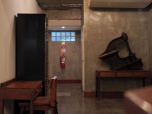 Un couloir avec une table et des chaises en bois, un extincteur et un grand objet sombre posé sur une table.