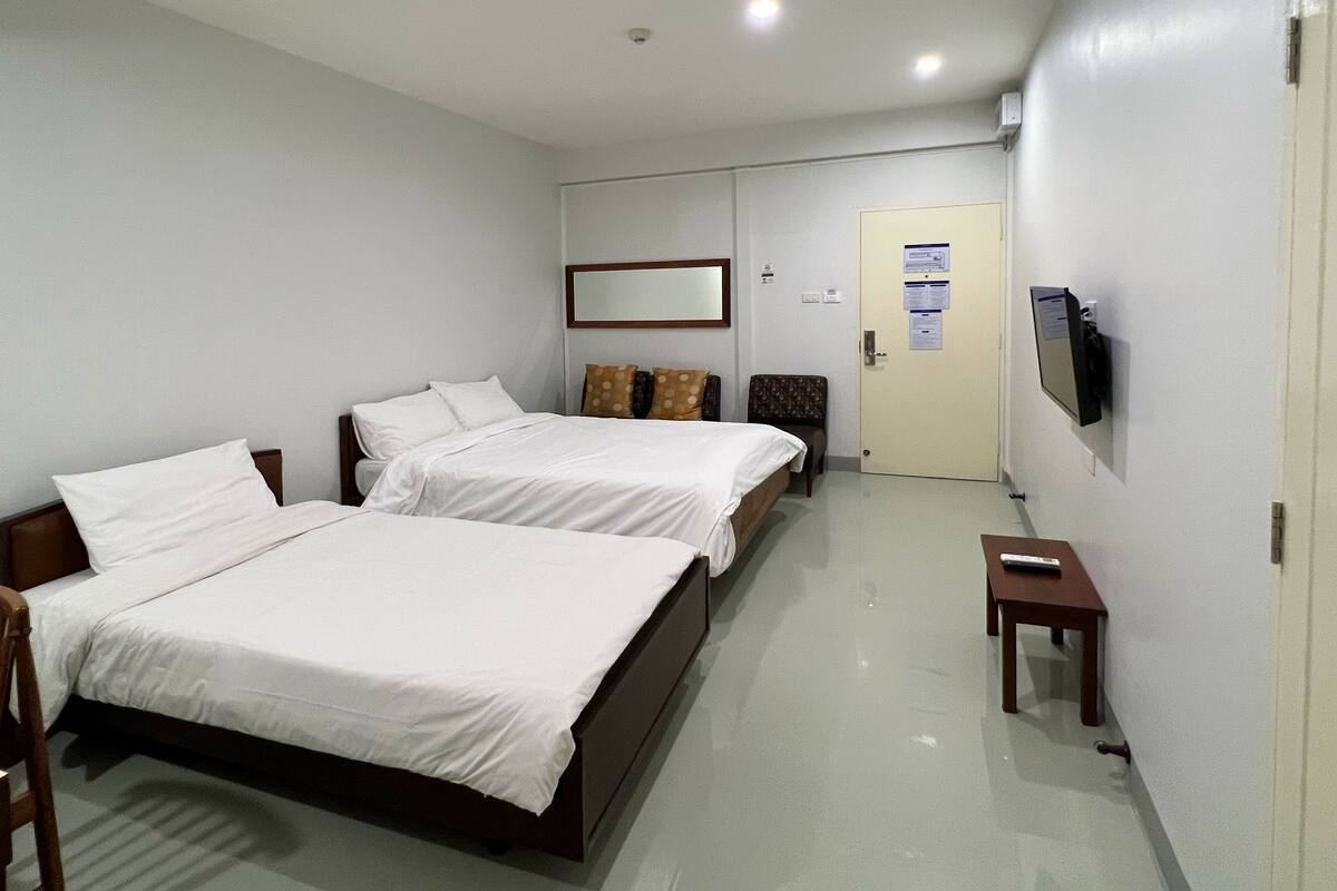 A hotel room with two beds, a TV mounted on the wall, and a door with a sign.