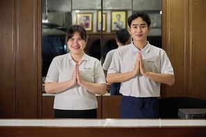 Two individuals in a hotel lobby with a wooden reception desk and framed pictures on the wall. - Niagara Hotel (Bangkok)