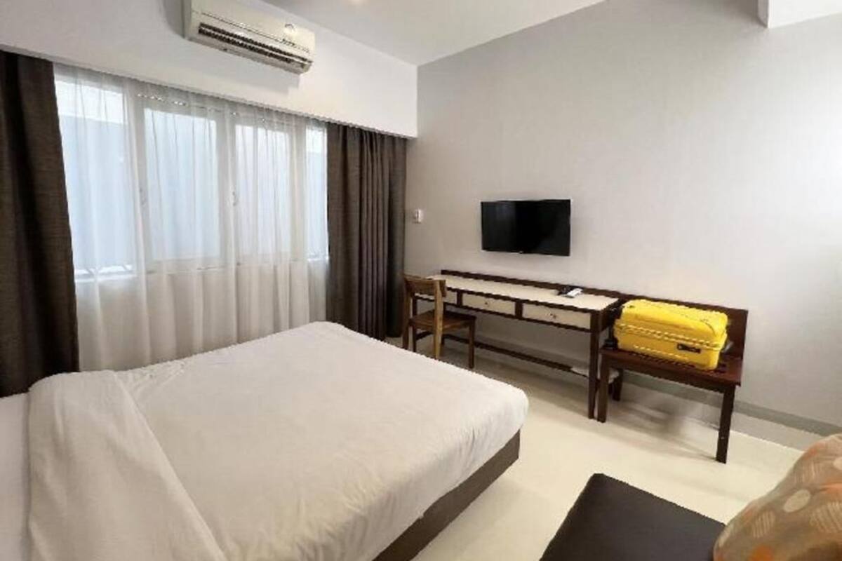 A hotel room with a bed, a desk, a chair, a television, and an air conditioning unit.