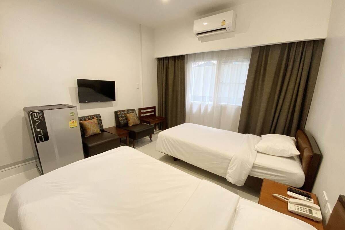 A hotel room with two beds, a TV, a refrigerator, a desk with a phone, and a window with curtains.
