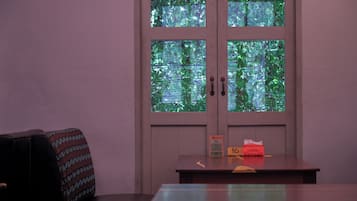 Um quarto com porta para uma varanda, uma mesa com um aviso e uma cadeira estampada.