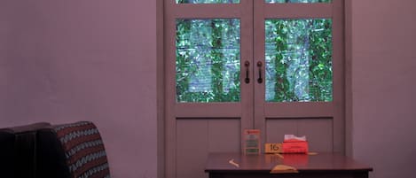 A room with a door leading to a balcony, a table with a sign, and a patterned chair.