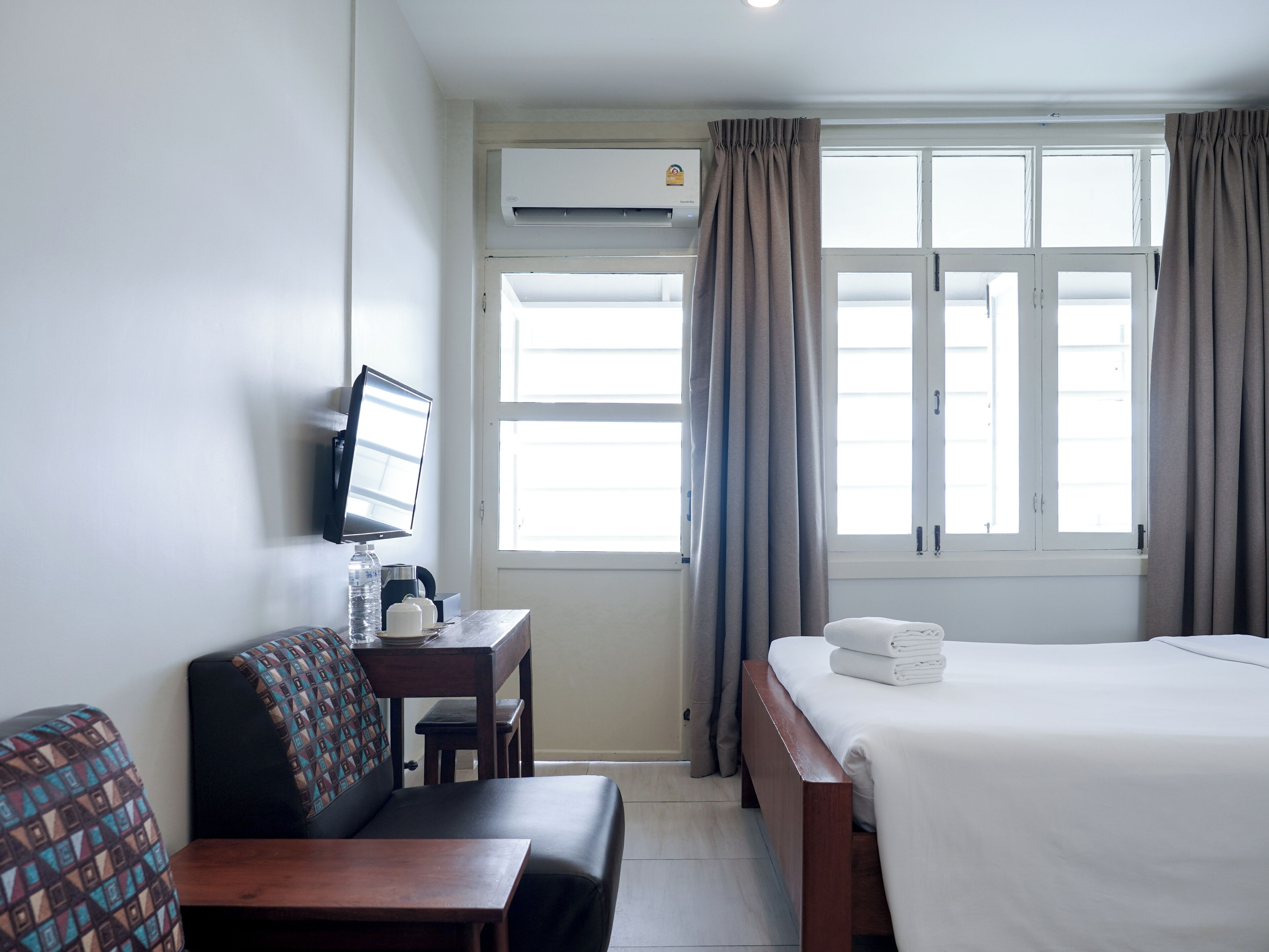 A hotel room with a bed, a desk with a computer, a chair, and a window with curtains.