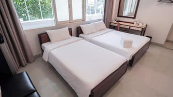 Quarto de hotel com duas camas, uma mesa de cabeceira com espelho e uma janela com cortinas.
