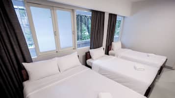 Quarto de hotel com três camas de solteiro, uma janela grande com cortinas e vista para o verde lá fora.