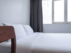 A neatly made bed with white linens in a room with a window and a curtain. - Niagara Hotel (Bang Rak)