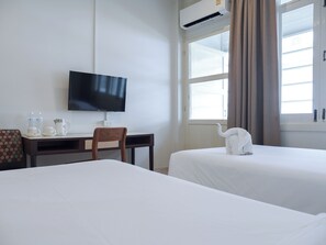 A hotel room with a TV, a desk with a chair, two beds, and a window with curtains. - Niagara Hotel (Bangkok)