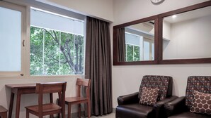 A room with a wooden desk, two chairs, a sofa with patterned cushions, a mirror, and a window with curtains. - Niagara Hotel (Bangkok)