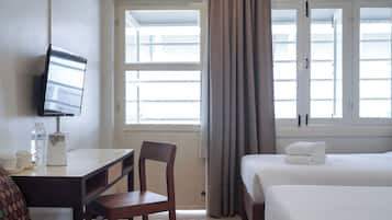 Habitación de hotel con cama, escritorio con silla, televisor y ventana con cortinas.