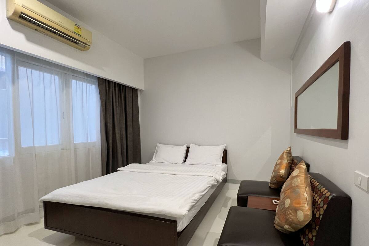 A modern bedroom with a bed, a sofa, a mirror, and an air conditioning unit.
